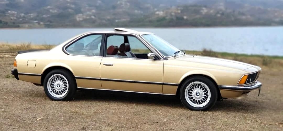 Gold BMW 6 Series E24 coupé parked beside a lake